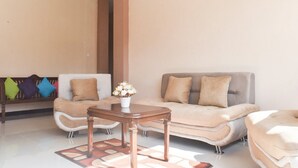 A living room with a sofa, a coffee table, and a bench with colorful cushions. - RedDoorz Syariah near Batu Night Spectacular (Batu)