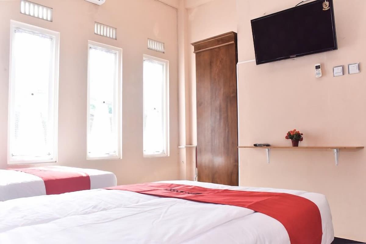 A hotel room with a bed, a television mounted on the wall, and a window with blinds.