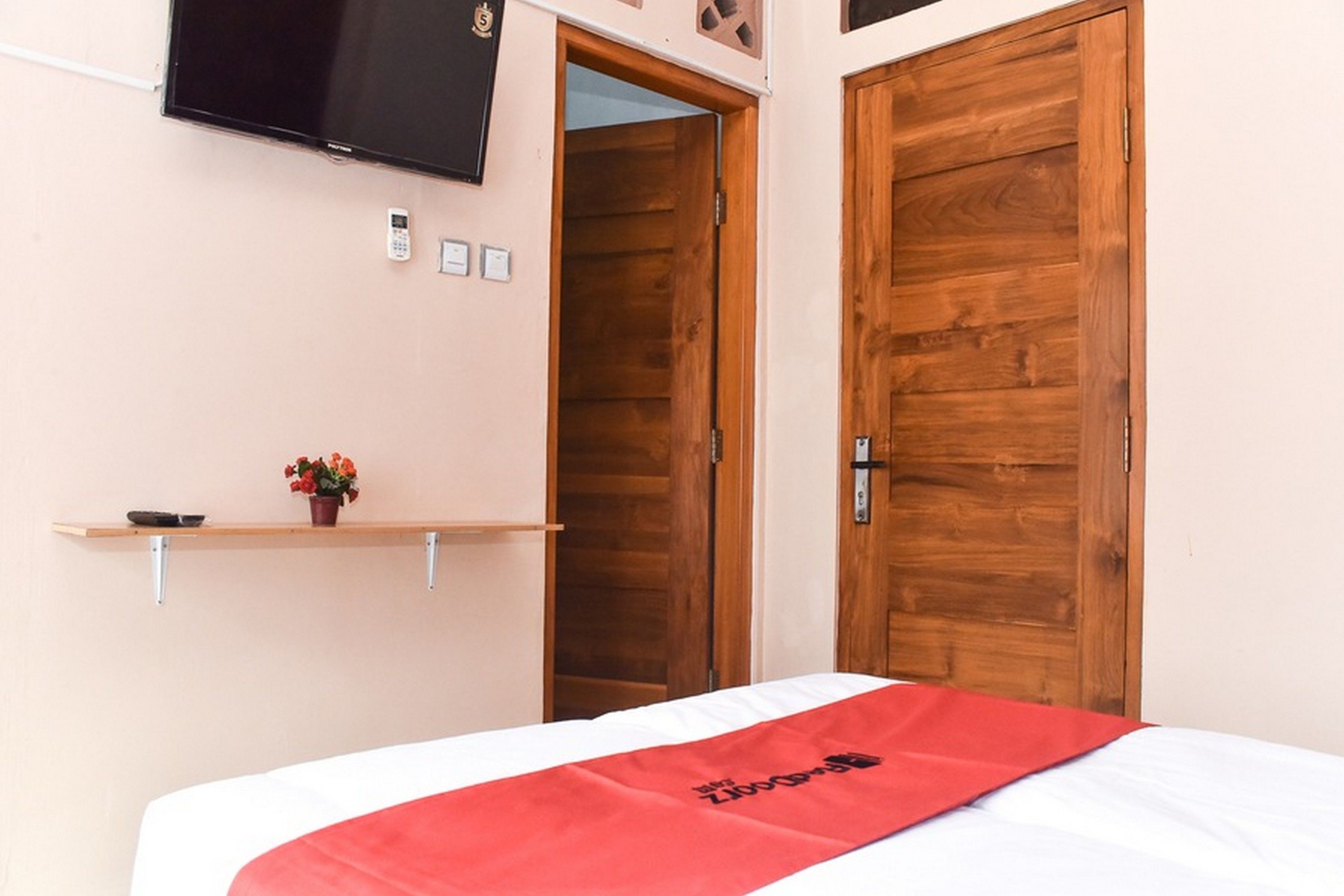 Een hotelkamer met een bed, een televisie aan de muur, een houten deur en een klein plankje met een plant.