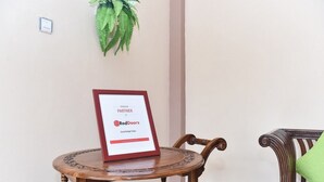 A framed sign on a wooden table in a room with a chair and a plant on the wall. - RedDoorz Syariah near Batu Night Spectacular (Batu)