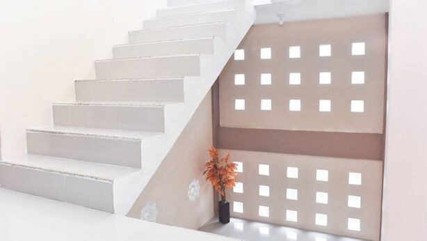 A staircase with white steps leading to a landing, a beige wall with a grid pattern, and a potted plant on the landing. - RedDoorz Syariah near Batu Night Spectacular (Batu)