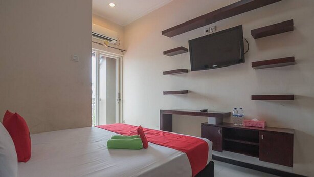 A hotel room with a bed, a TV mounted on the wall, and a small desk with a water bottle. - RedDoorz near E Walk Mall Balikpapan (Balikpapan)
