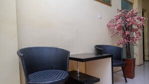 A corner with two wicker chairs and a small table, a potted plant with pink flowers, and a wall with a light switch. - RedDoorz @ Pengayoman Panakkukang 2 (Makassar)
