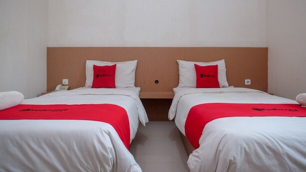 Two single beds with white bedding and red accents, a wooden headboard, and a small bedside table with a phone. - RedDoorz @ Pengayoman Panakkukang 2 (Makassar)