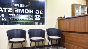 A reception area with three wicker chairs, a wooden reception desk, and a window displaying a sign with a phone icon. - RedDoorz @ Pengayoman Panakkukang 2 (Makassar)
