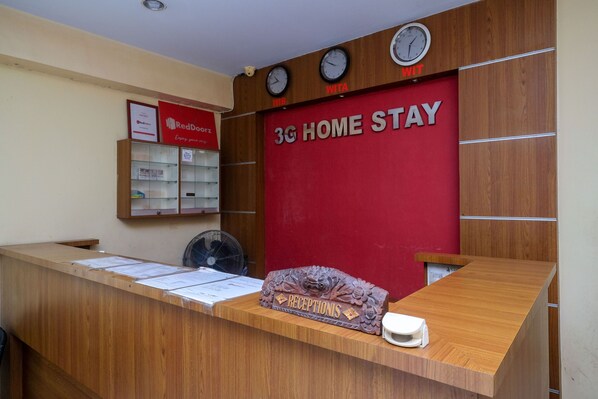A reception desk with a 3G home stay sign, clocks, and a fan. - RedDoorz @ Pengayoman Panakkukang 2 (Makassar)