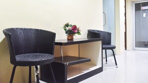 A small, modern room with a black sofa and a coffee table, a vase with flowers, and a door with a sign. - RedDoorz @ Pengayoman Panakkukang 2 (Makassar)
