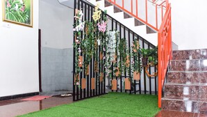 Una escalera con barandilla roja, un tapete de césped artificial verde y una pared decorativa con plantas.