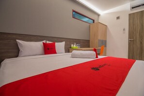 A hotel room with a large bed, a wooden headboard, a small window, a wardrobe, and a door.