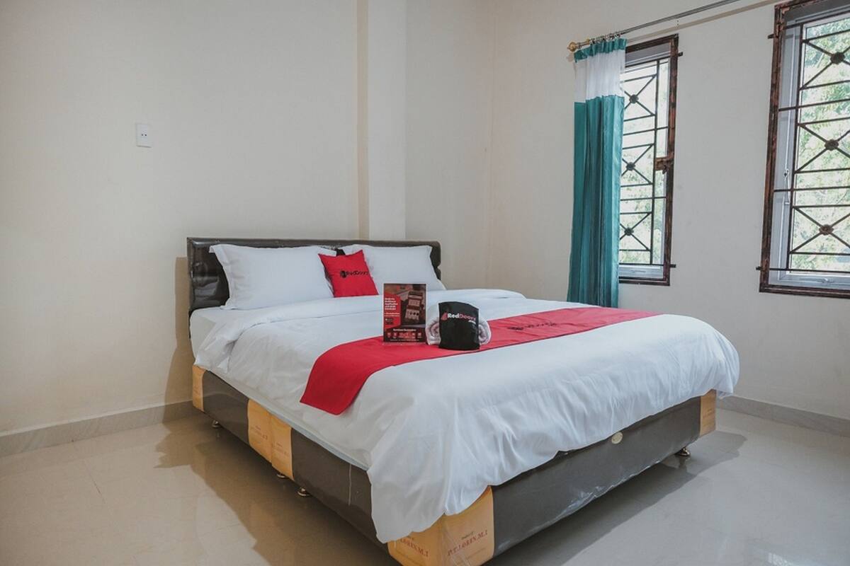 A neatly made bed with white bedding, a red throw, and a black mug on the nightstand.