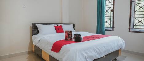 A neatly made bed with white bedding, a red throw, and a black mug on the nightstand.