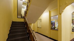 A staircase with black steps and a metal railing, leading to a landing with a yellow wall and a framed picture. - RedDoorz Plus near Ancol (Jakarta)