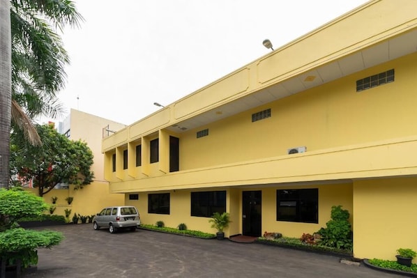 A yellow building with a covered parking area and a car parked in front. - RedDoorz Plus near Ancol (Jakarta)