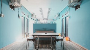 A narrow hallway with a central table and chairs, flanked by air conditioning units and windows. - RedDoorz near RSUD Koja (Jakarta)