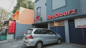 A building with a sign reading "RedDoorz" and a parked silver car in front. - RedDoorz near RSUD Koja (Jakarta)