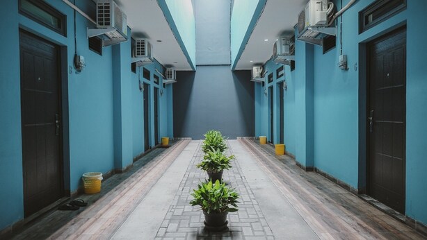 A hallway with blue walls, air conditioning units, and potted plants. - RedDoorz near RSUD Koja (Jakarta)