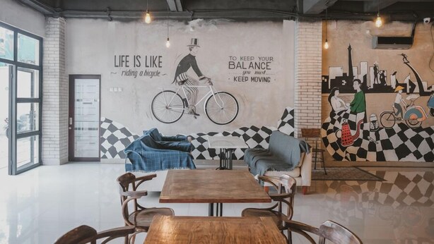 A modern cafe with a large mural, wooden furniture, and a checkered floor pattern. - RedDoorz near Plaza Atrium Senen (Jakarta)