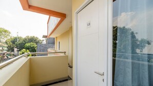 A corridor with a door marked '12', a balcony with a metal railing, and a view of greenery outside. - RedDoorz near Plaza Atrium Senen (Jakarta)