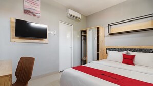 A hotel room with a bed, a television mounted on the wall, a wooden chair, and a wardrobe. - RedDoorz near Plaza Atrium Senen (Jakarta)