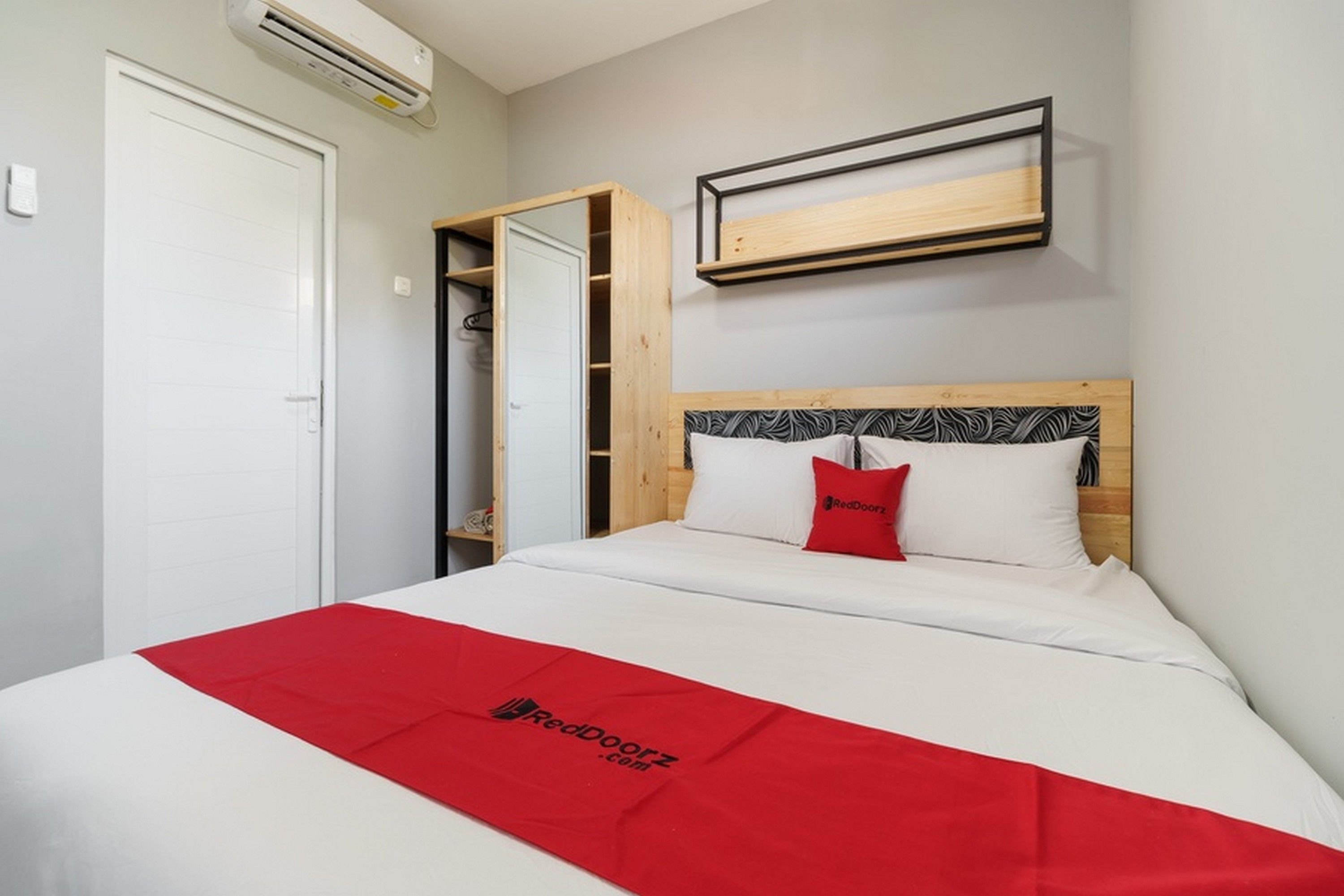 A hotel room with a bed, a wardrobe, and a shelf with a RedDoorz logo.