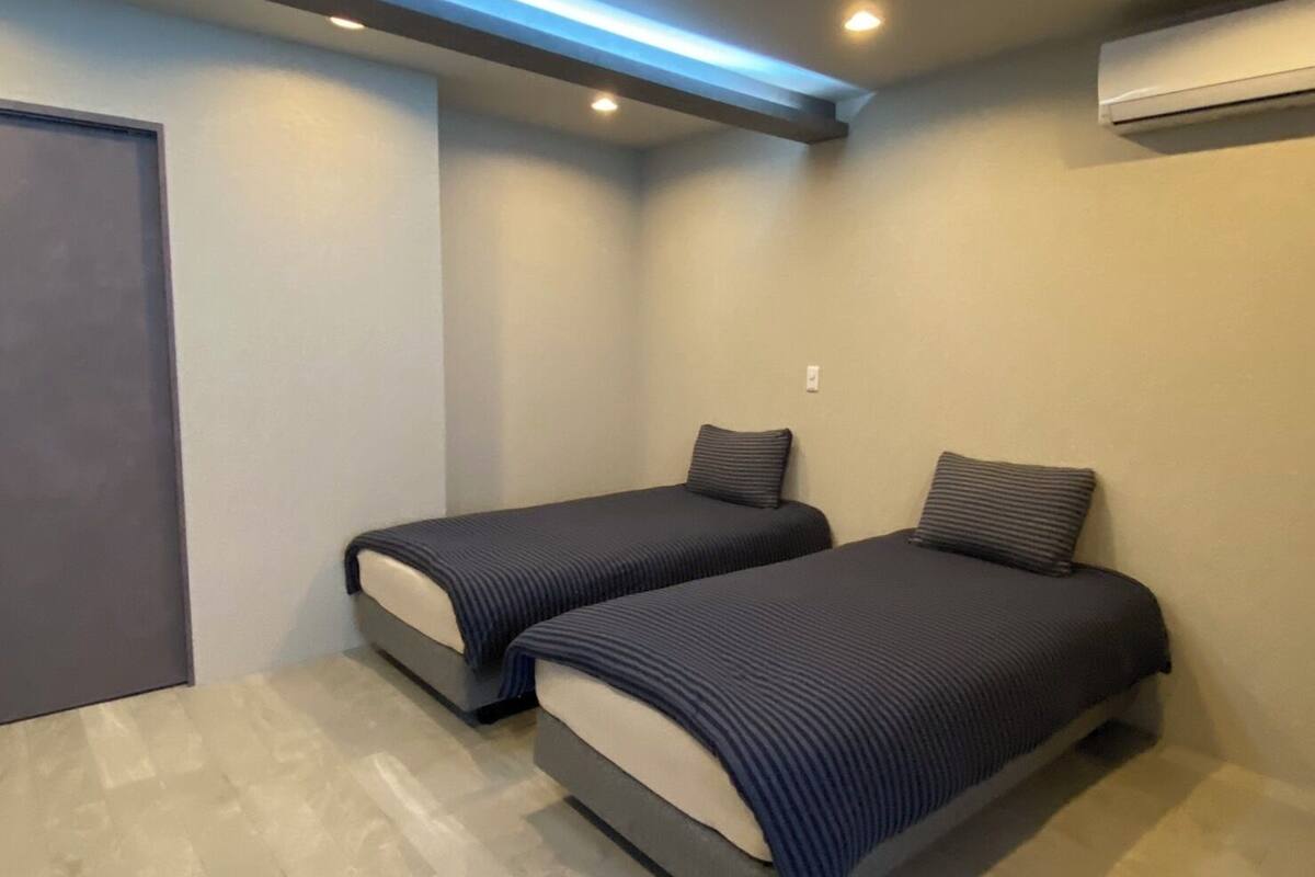 A small, modern bedroom with two single beds, a door, and an air conditioning unit on the wall.