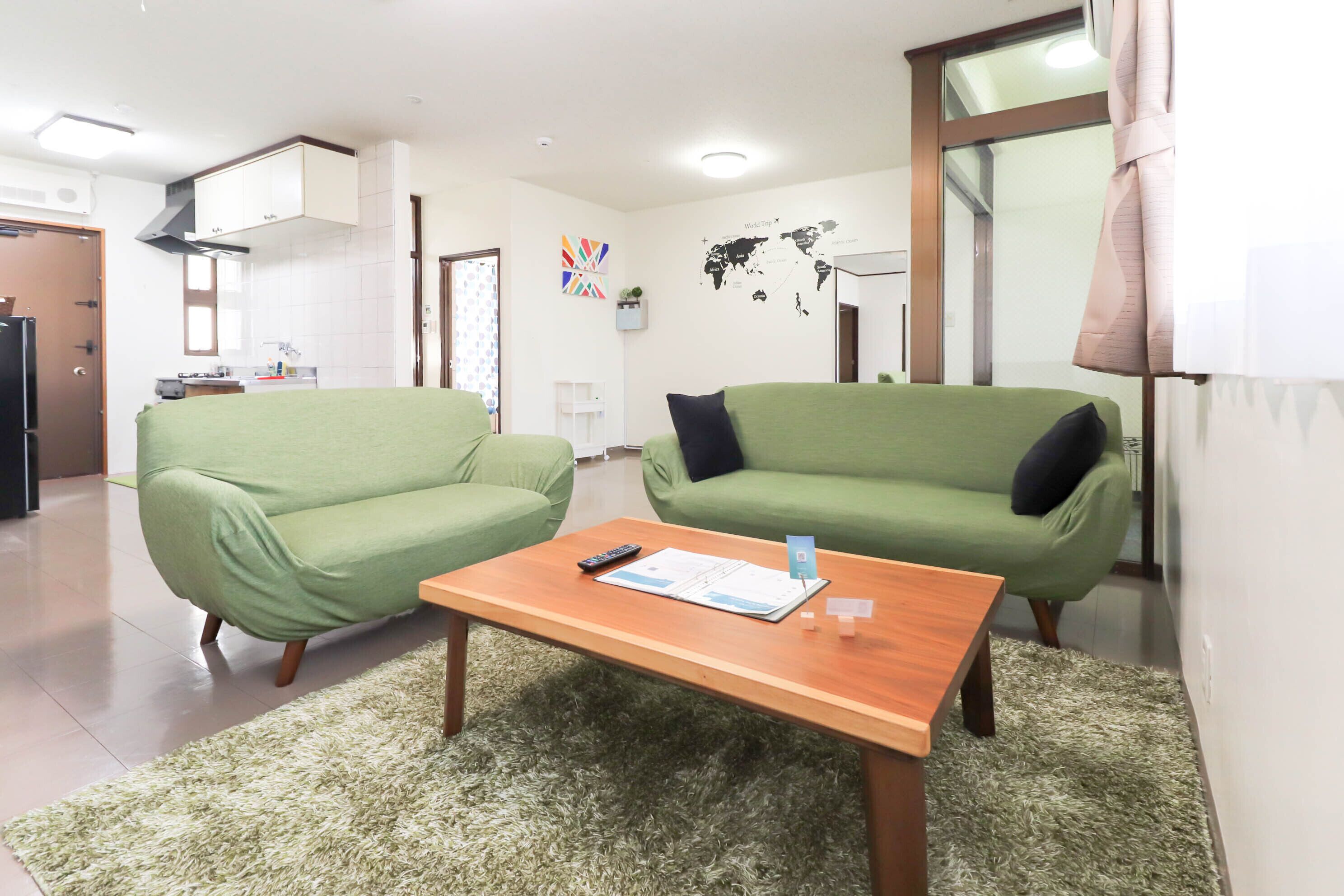 A living room with two green sofas, a wooden coffee table, and a world map on the wall.