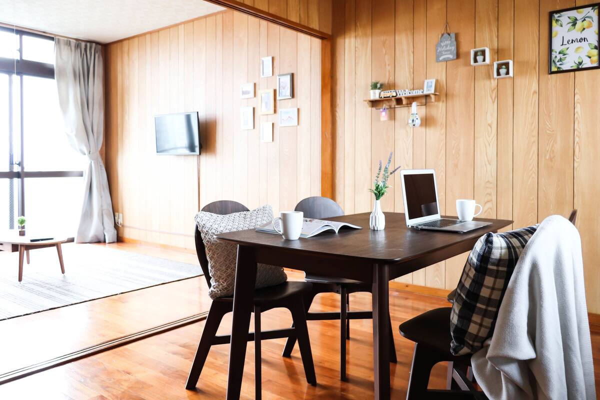 A wooden-paneled room with a dining table, chairs, a laptop, and a television.