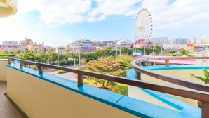 A balcony with a view of a cityscape, including a Ferris wheel and buildings. - Hotel Upi – Condominium Mihama (Chatan)