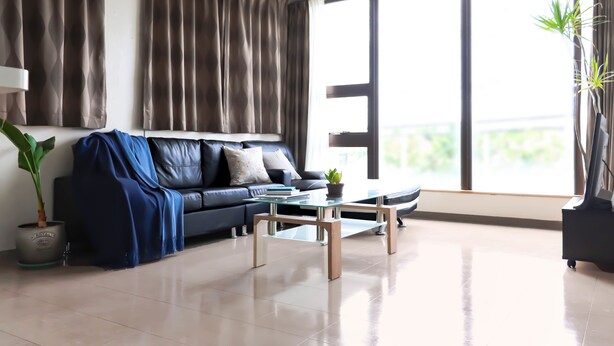 A modern living room with a leather sofa, a glass coffee table, and a large window with curtains. - Hotel Upi – Condominium Mihama (Chatan)