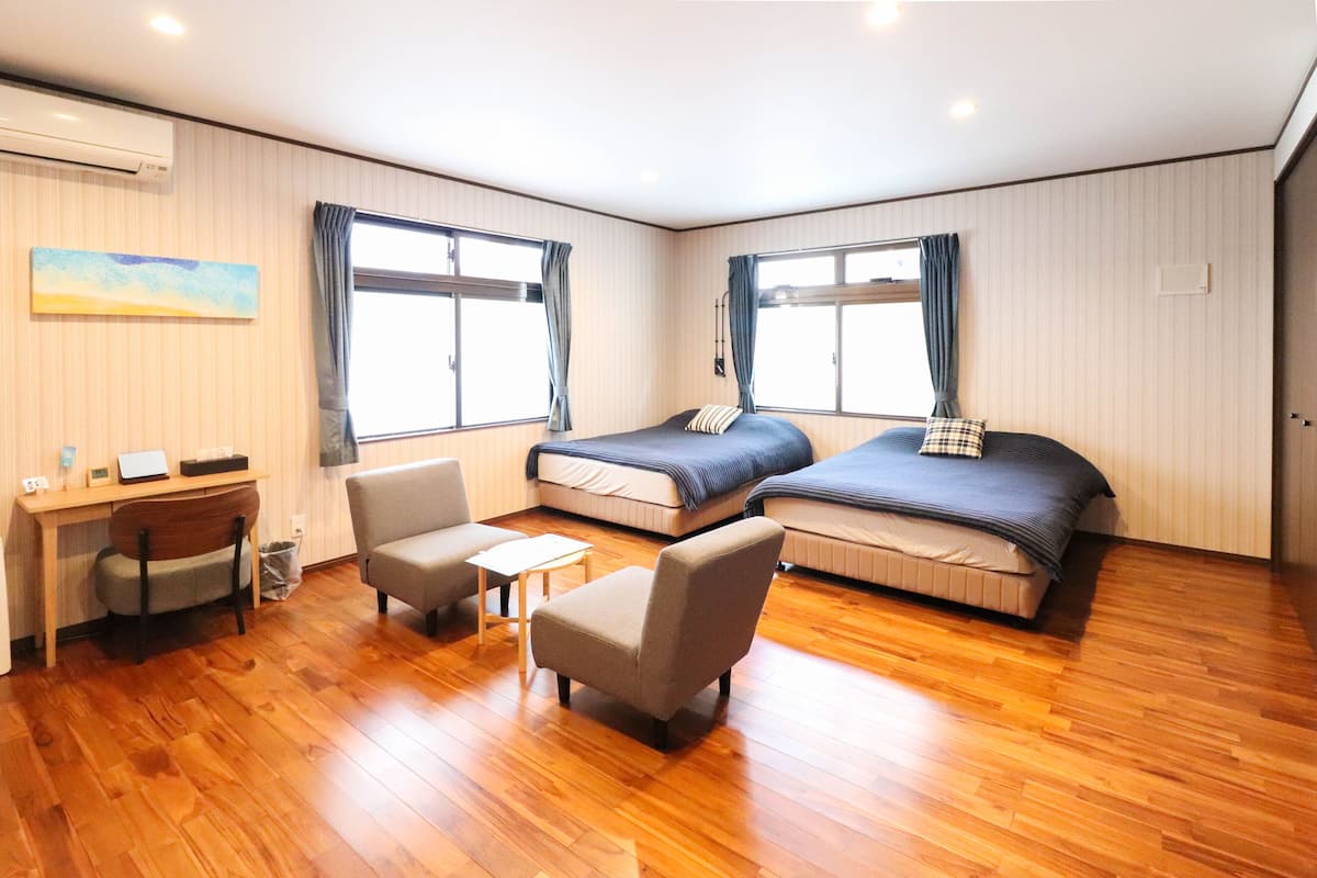 A hotel room with two beds, a desk, a chair, and a small table.