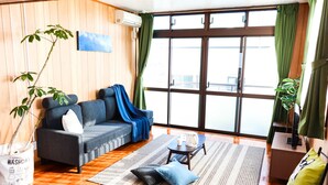 A modern living room with a sofa, coffee table, and a large window with curtains. - Hotel Upi – Condominium Mihama (Chatan)