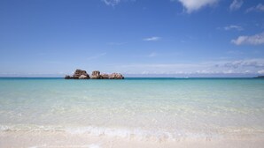 A beach with clear turquoise water and a rocky outcrop in the distance. - Hotel Upi – Condominium Mihama (Chatan)