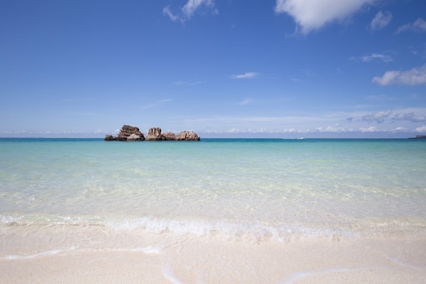 Una playa con agua turquesa cristalina y un promontorio rocoso en la distancia.