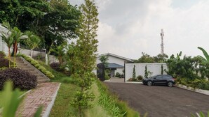 A modern building with a paved driveway and a parked car. - RedDoorz Plus near Exit Toll Puncak 2 (Ciawi)