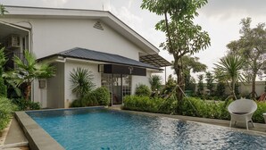 A modern building with a swimming pool, surrounded by lush greenery and a white chair. - RedDoorz Plus near Exit Toll Puncak 2 (Ciawi)