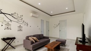 A modern living room with a grey sofa, a wooden coffee table, and a TV on a glass table. - RedDoorz Plus near Exit Toll Puncak 2 (Ciawi)
