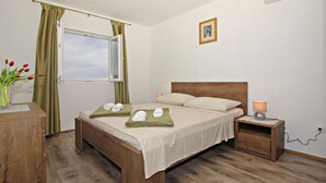 Une chambre avec un lit en bois, une table de chevet avec une lampe, une fenêtre avec des rideaux et un tableau au mur.
