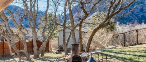 A patio with a table and chairs, surrounded by trees and a mountain view.