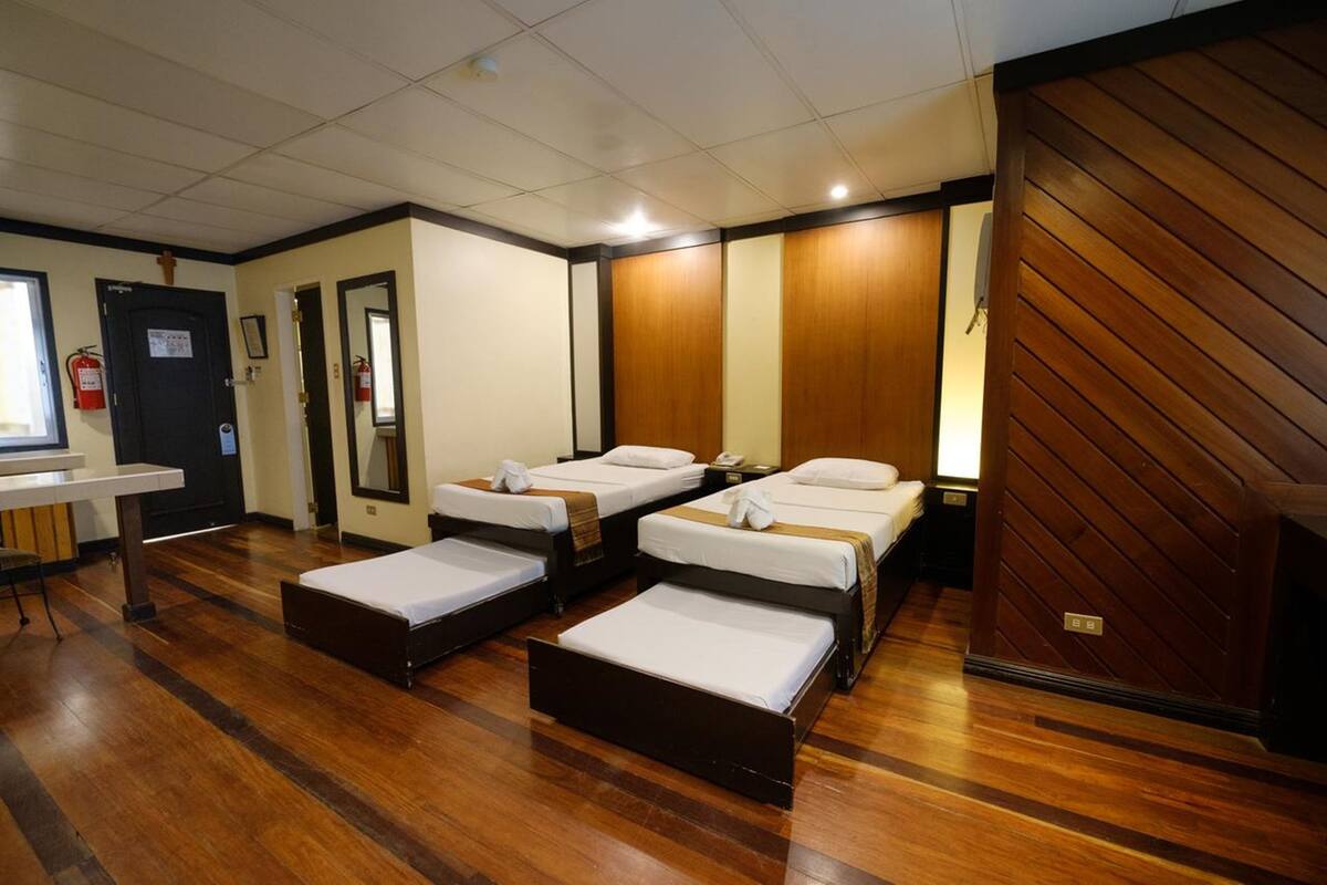 A hotel room with four single beds, a small table, and a wooden wall panel.