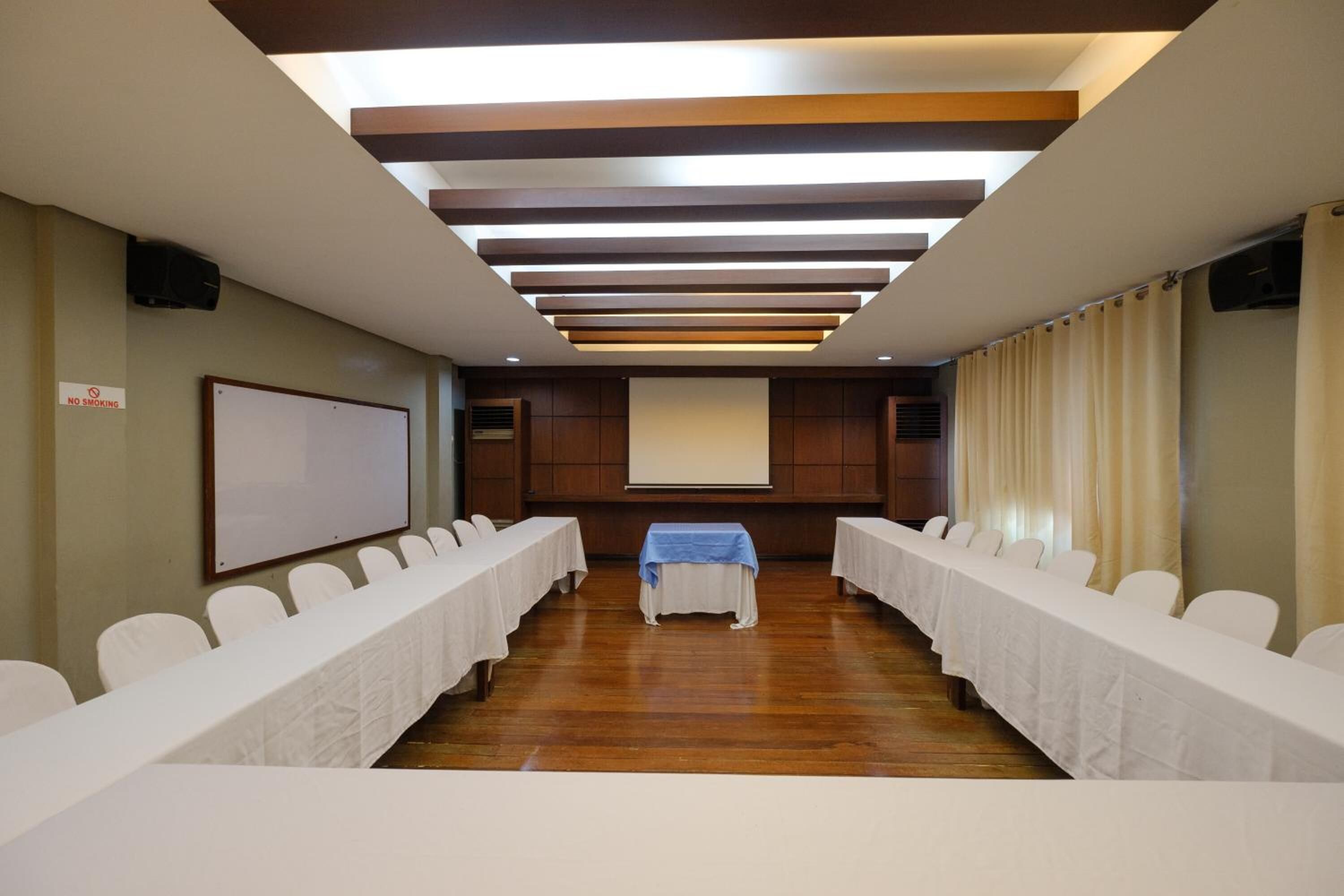 A conference room with a long table, white chairs, a projector screen, and a "No Smoking" sign.