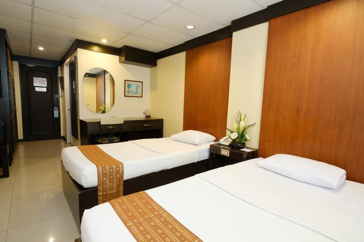 A hotel room with two beds, a desk, a mirror, and a wooden accent wall.