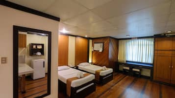 A hotel room with two single beds, a small desk with a refrigerator, a mirror, and a wardrobe.