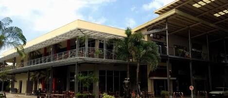 A hotel with a covered outdoor seating area, a central garden with a statue, and a car parked nearby.