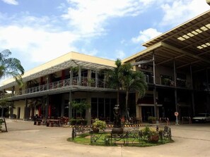 A hotel with a covered outdoor seating area, a central garden with a statue, and a car parked nearby.