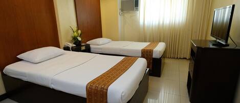 A hotel room with two beds, a television, a desk, and a fire exit sign.