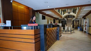 A hotel reception area with a wooden reception desk, a staircase in the background, and a seating area with tables and chairs. - Lispher Inn (Davao)