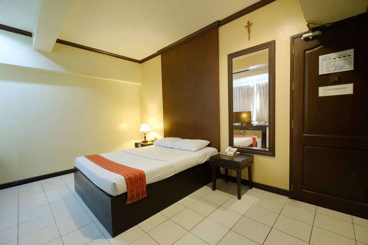 A hotel room with a bed, bedside table, lamp, and a mirror.