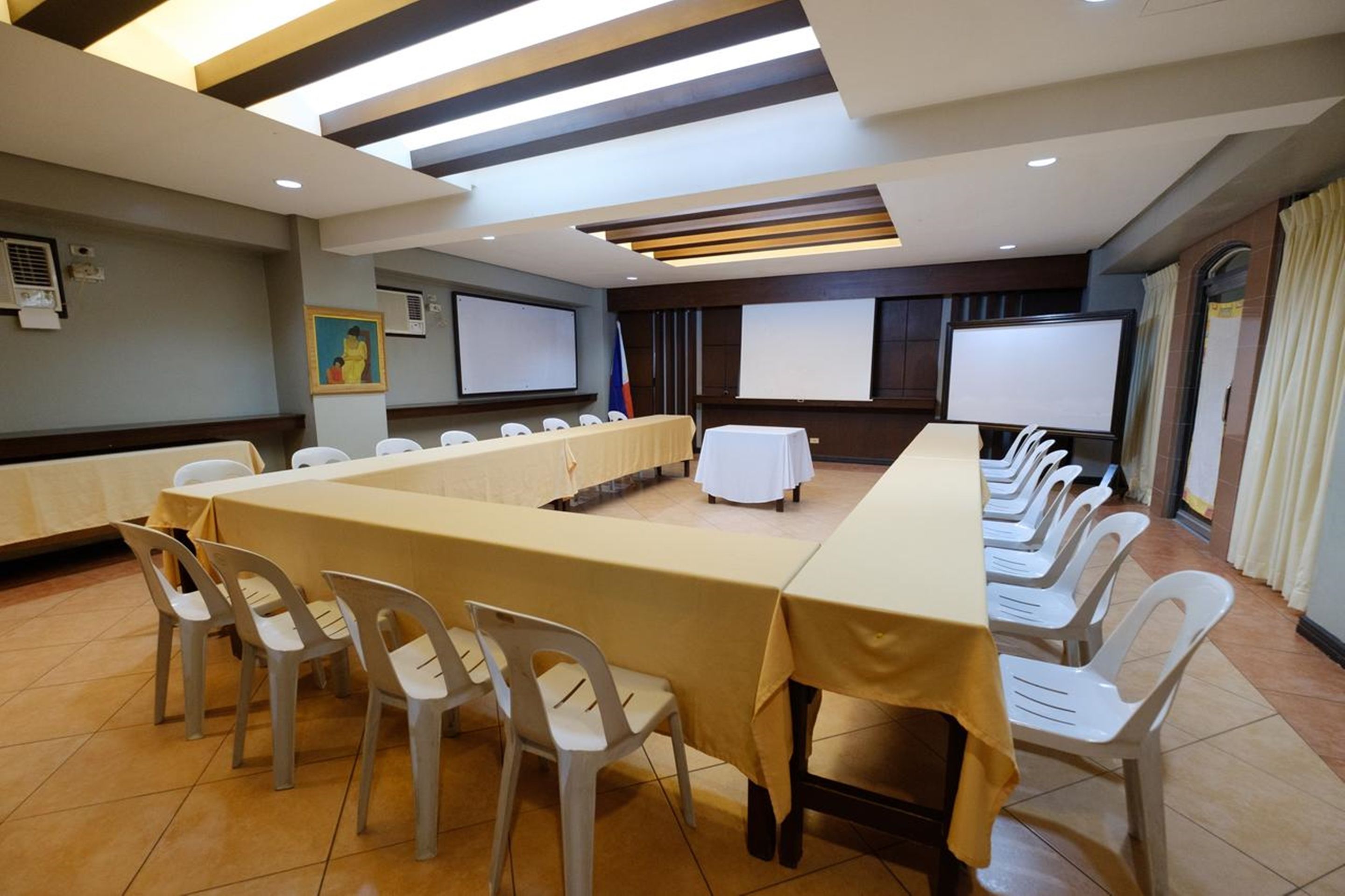 A conference room with a long table, white chairs, and a projector screen.