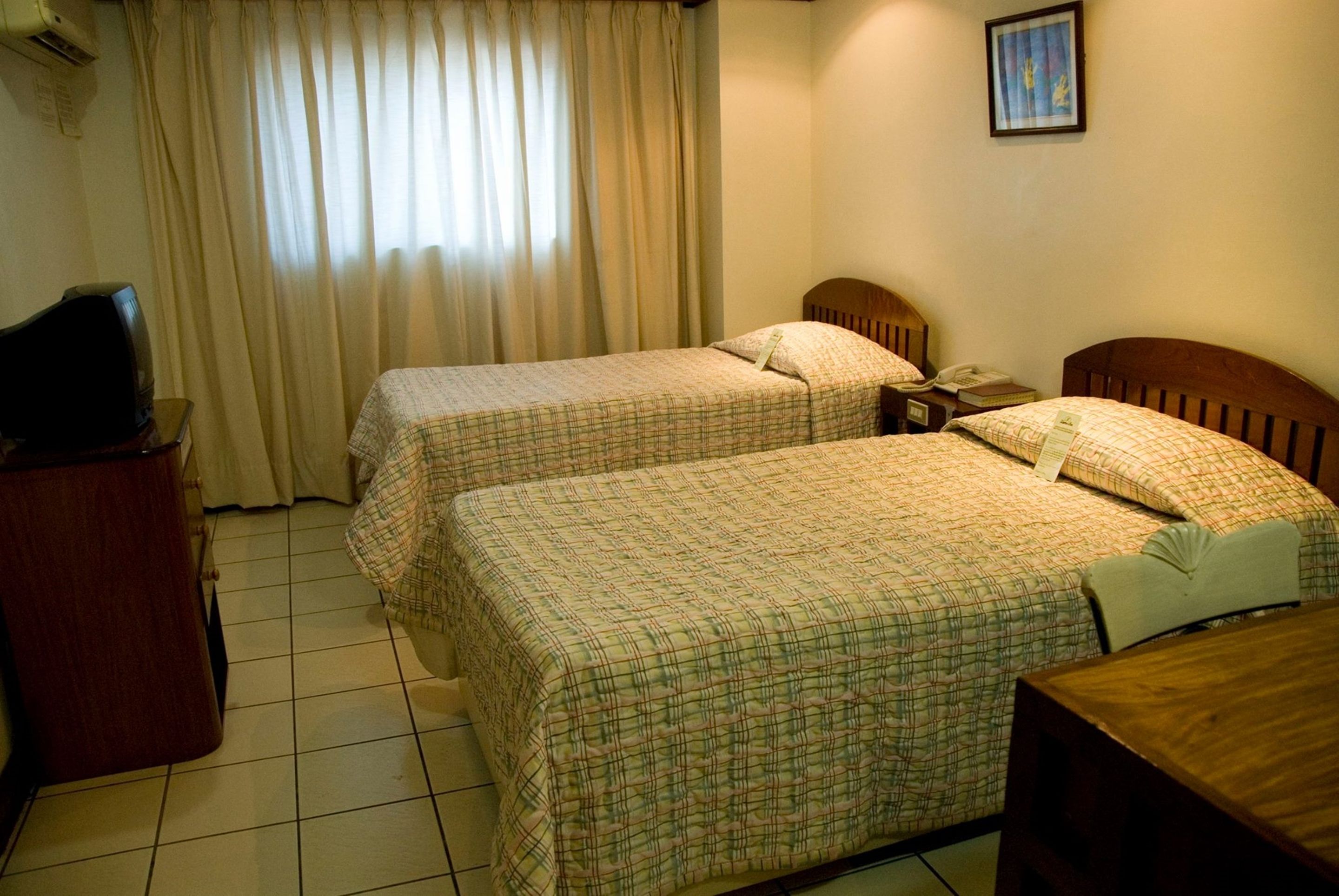 Une chambre d’hôtel avec deux lits, un bureau, une télévision et une fenêtre avec des rideaux.