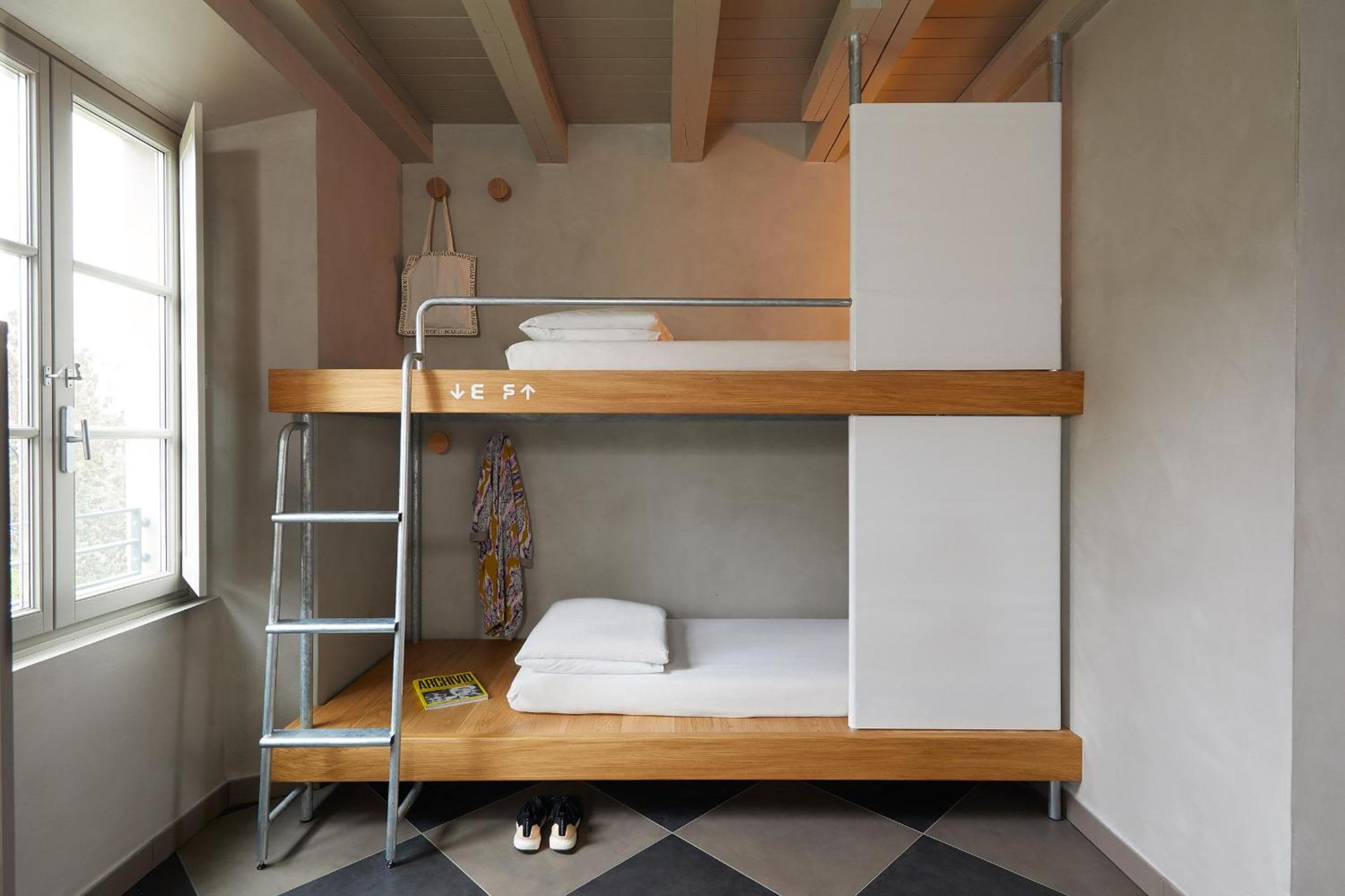 Una cama litera con escalera, una mesita con un libro y un par de zapatos en el suelo.